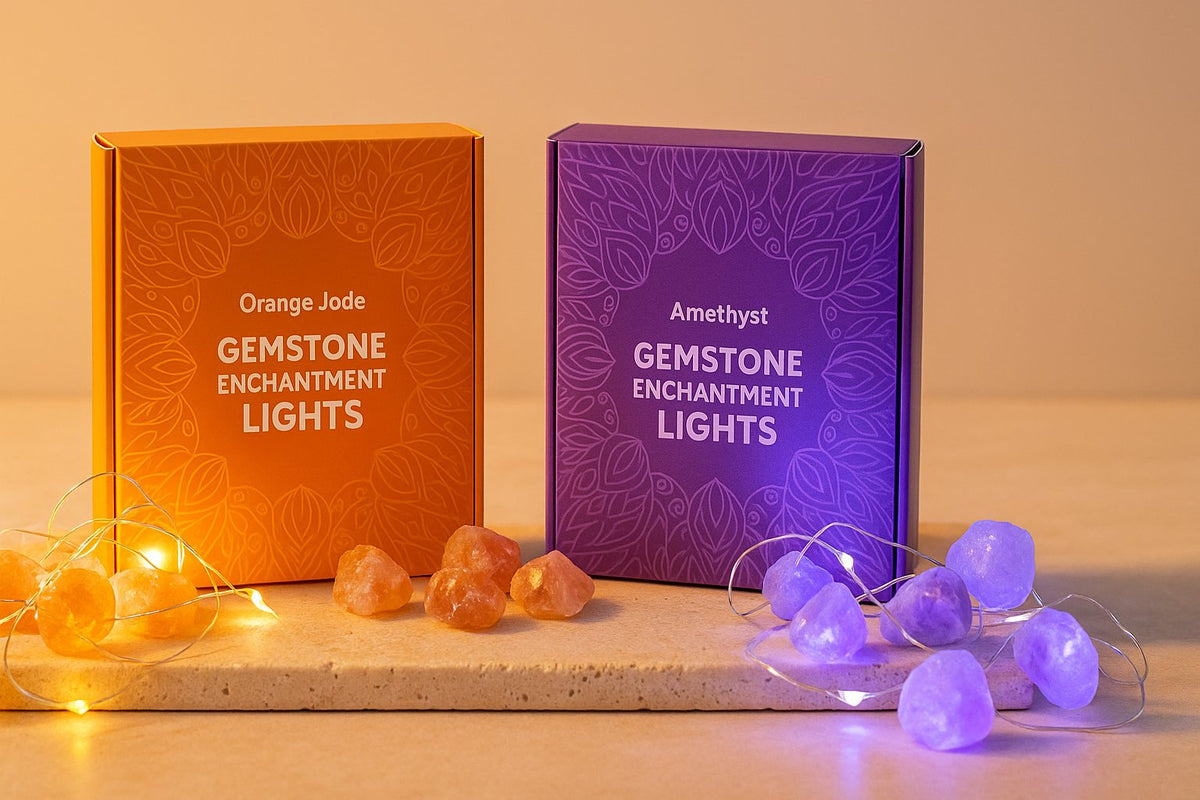 Portada de colección luces encantadas con dos cajas (Orange Jade y Amethyst) y guirnaldas LED sobre travertino beige, fondo melocotón y luz cálida.