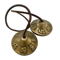 Tingsha tibetana: címbalos de bronce 6 cm con cuero; símbolos de suerte grabados; sonido claro para purificación y relajación.
